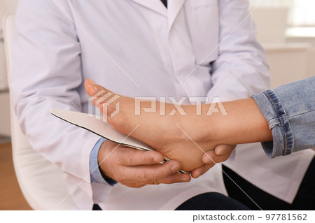 Male orthopedist fitting insole on patient's foot in clinic, closeup Male orthopedist fitting insole on patient's foot in clinic, closeup 97781562