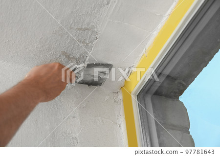Man plastering window area with putty knife indoors, closeup. Interior repair Man plastering window area with putty knife indoors, closeup. Interior repair 97781643