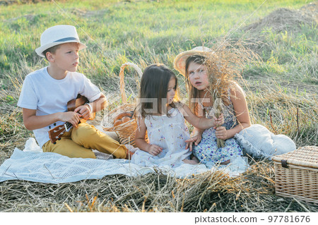 Premium Photo  Portrait of glad three kids sitting on blanket in field  playing ukulele having picnic with drinks and tasty food