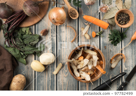 Composition of brown wooden bowl with potato peelings, little bowl with peppercorns, peeled potatoes, carrot, onion. 97782499