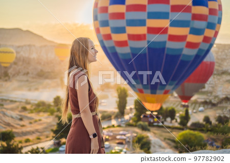 Tourist woman looking at hot air balloons in Cappadocia, Turkey. Happy Travel in Turkey concept. Woman on a mountain top enjoying wonderful view 97782902