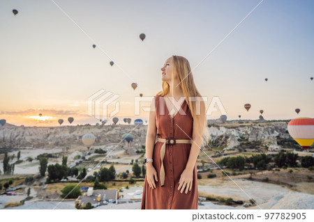 Tourist woman looking at hot air balloons in Cappadocia, Turkey. Happy Travel in Turkey concept. Woman on a mountain top enjoying wonderful view Tourist woman looking at hot air balloons in Cappadocia, Turkey. Happy Travel in Turkey concept. Woman on a mountain top enjoying wonderful view 97782905