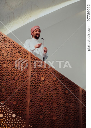 Muslims arabic Imam has a speech on friday afternoon prayer in mosque. Muslims have gathered for the friday afternoon prayer in mosque and are listening to the speech of imam Muslims arabic Imam has a speech on friday afternoon prayer in mosque. Muslims have gathered for the friday afternoon prayer in mosque and are listening to the speech of imam 97786022