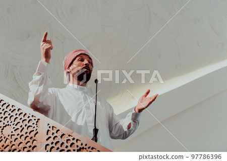 Muslims arabic Imam has a speech on friday afternoon prayer in mosque. Muslims have gathered for the friday afternoon prayer in mosque and are listening to the speech of imam 97786396