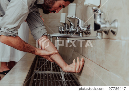 A Muslim performing ablution. Ritual religious cleansing of Muslims before performing prayer. The process of cleansing the body before prayer A Muslim performing ablution. Ritual religious cleansing of Muslims before performing prayer. The process of cleansing the body before prayer 97786447
