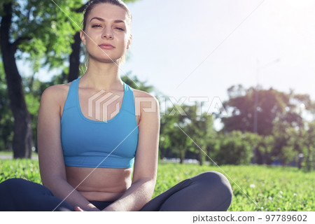 Girl meditates in lotus pose on green grass Girl meditates in lotus pose on green grass 97789602