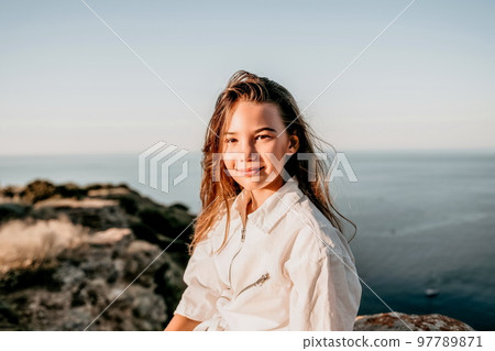 Adorable teenage girl outdoors enjoying sunset at beach on summer day. Close up portrait of smiling young romantic teenager girl with long hair on beach at summer evening. Travel and holidays 97789871