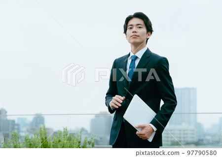 Businessman standing with a computer on the roof Businessman standing with a computer on the roof 97790580
