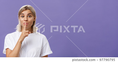 Charming creative and stylish beautiful tanned girl with fair hair shushing at camera with delighted thrilled look making up great idea wanting hide it and keep secret posing over purple wall Charming creative and stylish beautiful tanned girl with fair hair shushing at camera with delighted thrilled look making up great idea wanting hide it and keep secret posing over purple wall 97790795