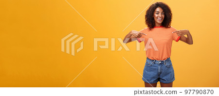 Hey pick me I your girl looking for. Portrait of charming friendly-looking ambitious dark-skinned female with afro hairstyle pointing at chest proudly and joyful posing against orange background Hey pick me I your girl looking for. Portrait of charming friendly-looking ambitious dark-skinned female with afro hairstyle pointing at chest proudly and joyful posing against orange background 97790870