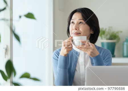 一個在電腦工作間隙喝咖啡的中年婦女 97790886