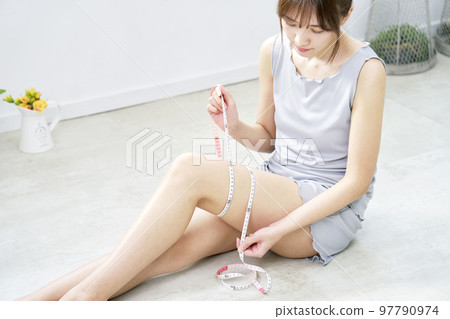 A woman measuring her thigh with a tape measure A woman measuring her thigh with a tape measure 97790974