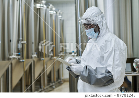 African American worker in protective costume working online on tablet pc while standing in workshop African American worker in protective costume working online on tablet pc while standing in workshop 97791243
