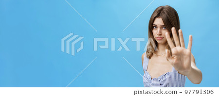 Silly and shy insecure attractive girl pulling hand towards to cover face from camera making moody timid expression asking to stop not liking what happening saying no with body language over blue wall Silly and shy insecure attractive girl pulling hand towards to cover face from camera making moody timid expression asking to stop not liking what happening saying no with body language over blue wall 97791306