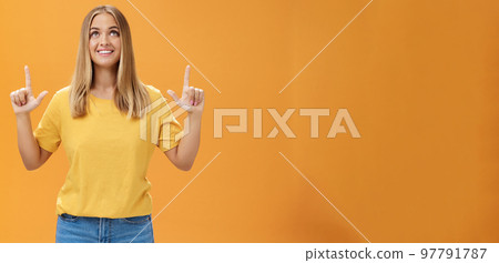 Portrait of upbeat joyful beautiful young caucasian girl with tan and fair hair looking and pointing up, smiling cheerfully watching fireworks posing amused and happy against orange background 97791787