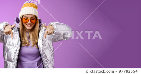 Joyful stylish blond woman in silver jacket stylish sunglasses jat enjoying perfect mountains view snowy vacation resort look pointing down smiling amused having fun feel happy, purple background Joyful stylish blond woman in silver jacket stylish sunglasses jat enjoying perfect mountains view snowy vacation resort look pointing down smiling amused having fun feel happy, purple background 97792554
