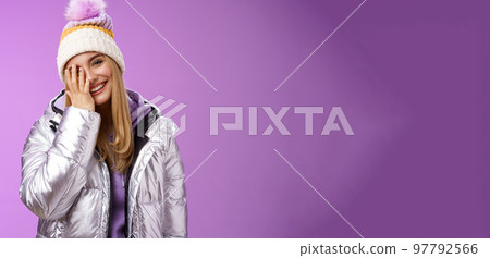 Carefree happy upbeat charming blond woman cover half face tilting head laughing joyfully wearing outdoor stylish silver jacket winter hat having fun awesome five star ski resort, purple background 97792566
