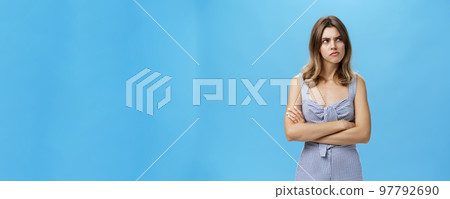Studio shot of woman thinking seriously being suspicious and hesitant pursing lips holding hands crossed on chest looking at upper right corner with frown, thinking over blue background 97792690