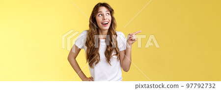 Wondered impressed charismatic fascinated smiling happy girl pointing look upper left corner speechless surprised grinning toothy happiness joy expression contemplate great view yellow background Wondered impressed charismatic fascinated smiling happy girl pointing look upper left corner speechless surprised grinning toothy happiness joy expression contemplate great view yellow background 97792732