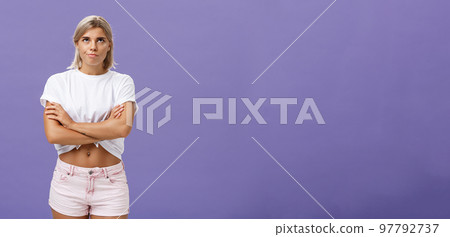 Girl being irritated waiting for appointment sighing rolling eyes up from annoyance crossing hands over body and smirking from impatience and dissatisfaction standing intense over purple wall 97792737