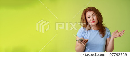 Well meh. Indifferent careless hesitant redhead middle-aged woman mature red female shrugging hold smartphone smirk bored uninterested hold hand aside apathetic attitude green background 97792739