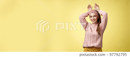 Nice charming playful young european female having fun, playing mimicking bunny showing rabbit ears with hands behind head, smiling cute, tender, happy greeting boyfriend welcome back ove yellow wall 97792795