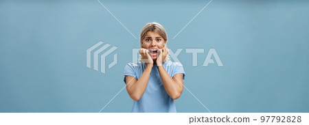 Indoor shot of shocked troubled girlfriend hearing mom returned home being with boyfriend biting fingernails being in helpless perplexed situation feeling anxious and scared over blue background Indoor shot of shocked troubled girlfriend hearing mom returned home being with boyfriend biting fingernails being in helpless perplexed situation feeling anxious and scared over blue background 97792828