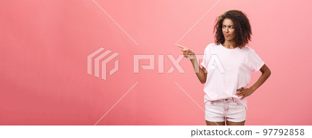 Picky fashionable and attractive young female stylist with curly hairstyle frowning and pouting with dislike and doubt looking and pointing left unsure having hesitation look fits customer Picky fashionable and attractive young female stylist with curly hairstyle frowning and pouting with dislike and doubt looking and pointing left unsure having hesitation look fits customer 97792858
