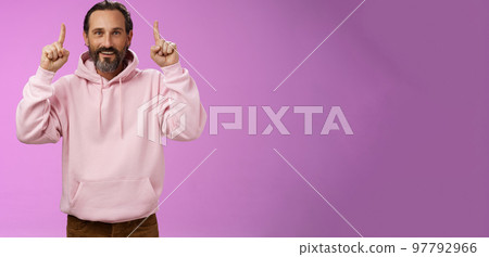 Handsome mature 50s man grey hair beard wearing stylish hipster loose hoodie pointing up index fingers showing awesome place hang out unwilling grow old standing positive lucky purple background 97792966