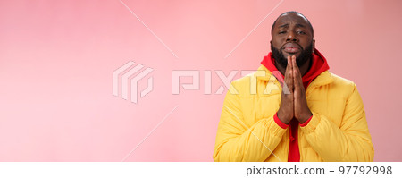 Miserable cute african-american bearded man in yellow coat asking help begging press palms supplicating apologizing please help, standing pink background sad need advice lending money 97792998