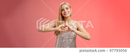 Romantic passionate charming lovely blond glamour woman in silver dress brilliants show heart love gesture express sympathy passion, adore relationship smiling delighted, standing red background 97793056
