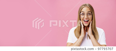 Woman liking new glasses picked in store feeling happy finding right frame touching cheeks from happiness smiling cheerfully at camera wearing transparent eyewear and t-shirt over pink wall Woman liking new glasses picked in store feeling happy finding right frame touching cheeks from happiness smiling cheerfully at camera wearing transparent eyewear and t-shirt over pink wall 97793707