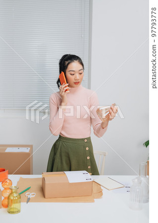 Young Asian woman owner of small online store packing customer orders in the home office. Young Asian woman owner of small online store packing customer orders in the home office. 97793778