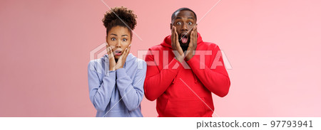 Amazed shocked gasping speechless two african american man woman drop jaw press palms cheeks worried nervous sympathizing terrible story standing stunned imrpessed pink background, feel sorry 97793941