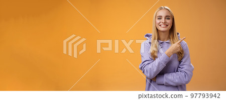 Charismatic modern millennial cute blond woman in hoodie smiling happily discussing cool new promo pointing right recommend check out visit interesting store near corner, orange background 97793942