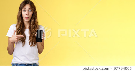 Intriguing app check out. Enthusiastic surprised attractive girlfriend gossiping friend new boyfriend showing curious photo smartphone hold mobile phone pointing telephone screen yellow background Intriguing app check out. Enthusiastic surprised attractive girlfriend gossiping friend new boyfriend showing curious photo smartphone hold mobile phone pointing telephone screen yellow background 97794005
