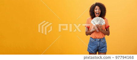 Woman cannot hide happiness winning lottery. Portrait of surprised and happy lucky african american young woman with curly hair holding bunch of money and yelling from delight receiving paycheck 97794168