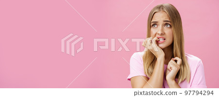 Girlfriend broke car feeling cocnerned and scared of man walking towards to argue looking aside with anxiety and panic biting fingernails from stress and troublesome situation posing over pink wall 97794294