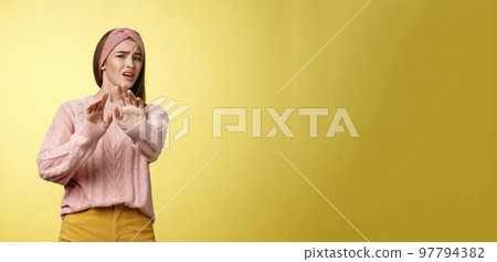 Omg no. Cute young european schoolgirl step back stooping grimacing disgusted and displeased turning away reluctant expressing aversion extending palm in rejection, refusal gesture over yellow wall 97794382