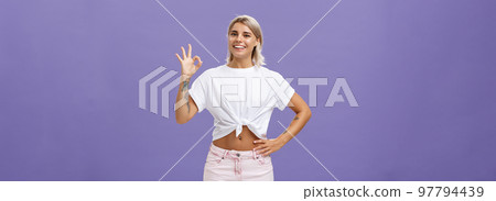 Excellent I like it. Portrait of satisfied good-looking happy girl with fair hair in white t-shirt and shorts showing ok or perfect gesture and smiling broadly holding hand on waist over purple wall Excellent I like it. Portrait of satisfied good-looking happy girl with fair hair in white t-shirt and shorts showing ok or perfect gesture and smiling broadly holding hand on waist over purple wall 97794439
