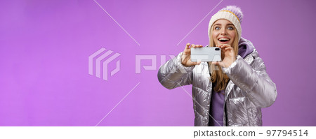 Amused fascinated female in silver jacket head smiling astonished excited look forward holding smartphone recording video taking shots famous person mobile phone camera, purple background Amused fascinated female in silver jacket head smiling astonished excited look forward holding smartphone recording video taking shots famous person mobile phone camera, purple background 97794514