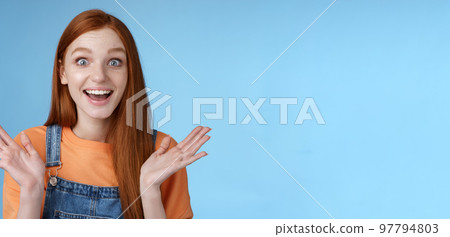 Surprised delighted happy friendly-looking amused redhead female friend learn incredible good news congratulating girlfriend fascinated wide eyes camera joyfully clap hands amazed, blue background 97794803