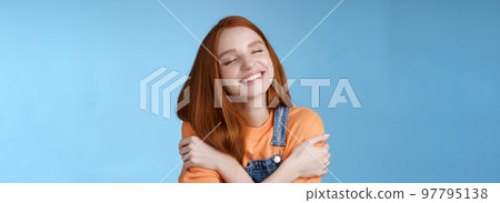 Close-up dreamy happy smiling redhead girl close eyes fantasizing romantic date grinning white teeth cuddle herself cross arms chest embracing recalling lovely memories hugging daydreaming 97795138