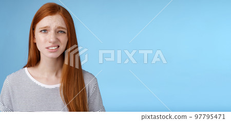 Displeased young awkward redhead girl cringe full disbelief smirking frowning confused look questioned doubtful hearing nuisance dumb story standing blue background uncertain Displeased young awkward redhead girl cringe full disbelief smirking frowning confused look questioned doubtful hearing nuisance dumb story standing blue background uncertain 97795471