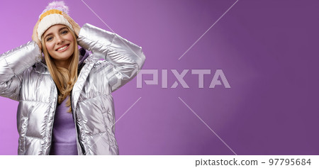 Tender romantic attractive blond female enjoying winter ski resort vacation having fun look pleased smiling broadly tilting head touching hat wearing silver stylish jacket, purple background Tender romantic attractive blond female enjoying winter ski resort vacation having fun look pleased smiling broadly tilting head touching hat wearing silver stylish jacket, purple background 97795684