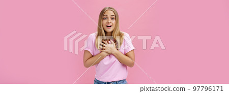 Indoor shot of touched surprised good-looking nice girl in t-shirt and jeans holding palms on heart gasping from amusement and amazement reacting to awesome pleasant news grateful and happy 97796171