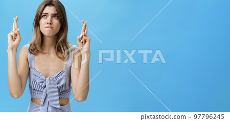 Waist-up shot of intense worried hopeful young woman waiting with anticipation for important result crossing fingers for good luck pursing lips from nervousness looking faithfully at upper left corner Waist-up shot of intense worried hopeful young woman waiting with anticipation for important result crossing fingers for good luck pursing lips from nervousness looking faithfully at upper left corner 97796245