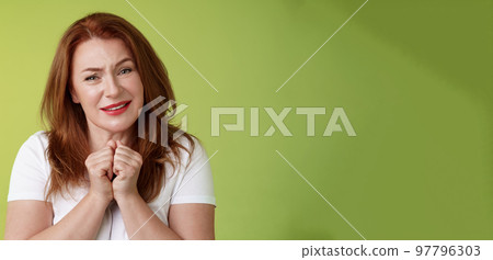 Silly touched tender redhead charmed middle-aged woman sighing gladly gaze admiration delighted press hands together heartwarmed fascinated look grateful lovely camera green background 97796303
