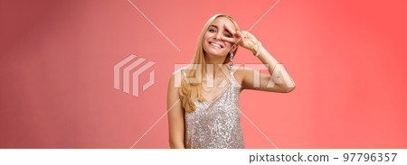 Optimistic lucky elegant european blond young 25s wife in silver glittering dress having fun enjoying celebration party dance floor showing peace victory sign eye smiling delighted, red background Optimistic lucky elegant european blond young 25s wife in silver glittering dress having fun enjoying celebration party dance floor showing peace victory sign eye smiling delighted, red background 97796357