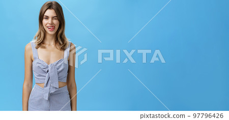Portrait of cute woman with natural hairstyle in matching clothes winking flirty showing tongue on upper lip and smiling tricky being in playful romantic mood feeling happy and joyful over grey wall Portrait of cute woman with natural hairstyle in matching clothes winking flirty showing tongue on upper lip and smiling tricky being in playful romantic mood feeling happy and joyful over grey wall 97796426